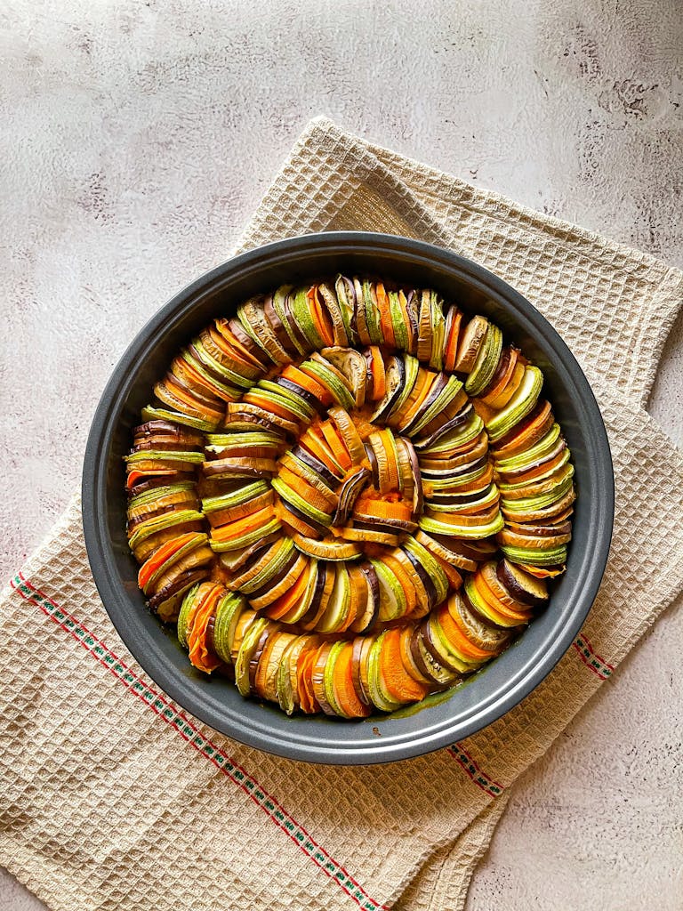 Top view of a vibrant vegetable tian dish in a round baking tray with zucchini and tomatoes.