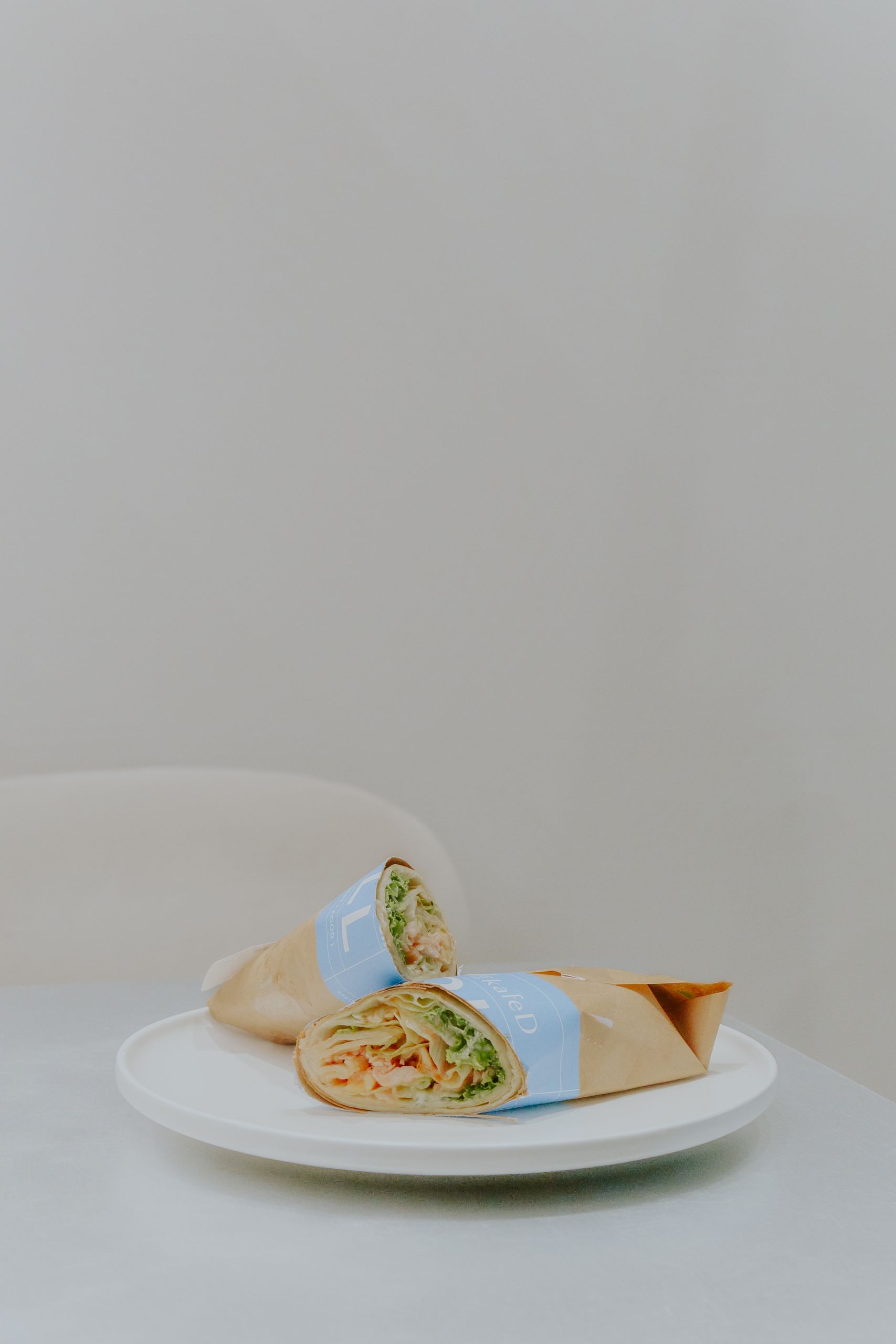 A fresh and tasty chicken wrap elegantly presented on a white plate with neutral background.