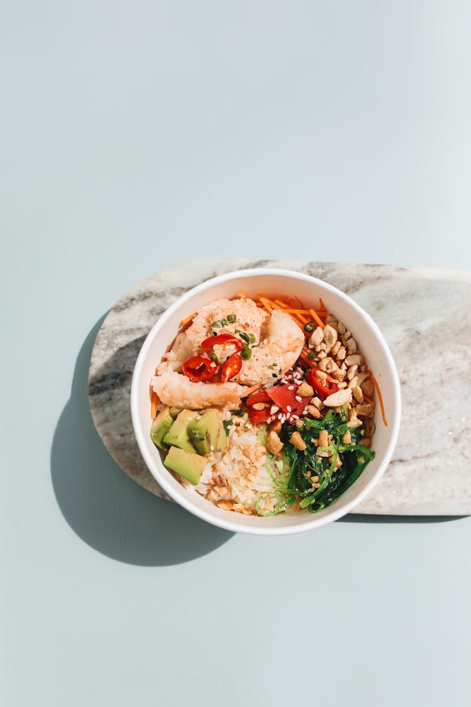 A fresh poke bowl featuring salmon, avocado, chili, and greens on a marble surface.