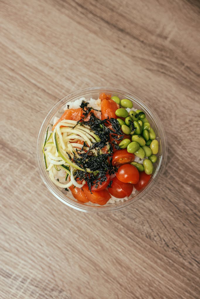 A top-down view of a nutritious salmon rice bowl with fresh veggies and seaweed on a wooden table.