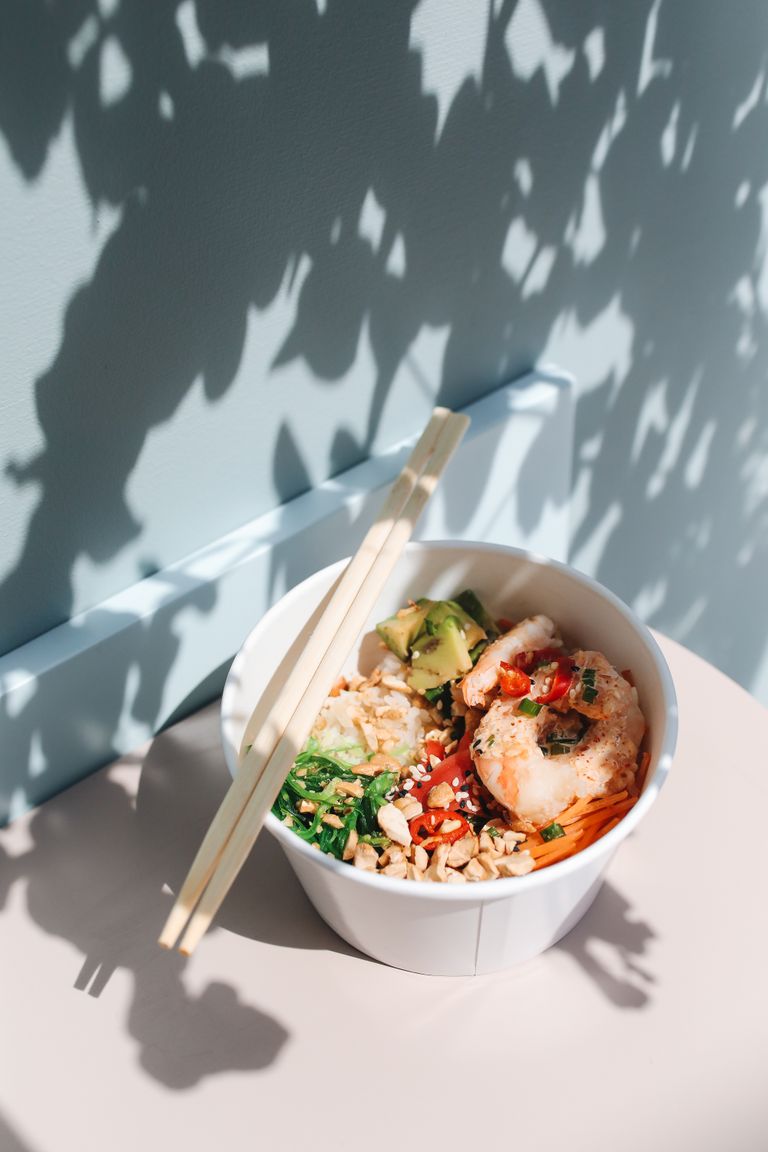 A vibrant poke bowl with shrimp and avocado, captured in artistic shadows by sunlight.