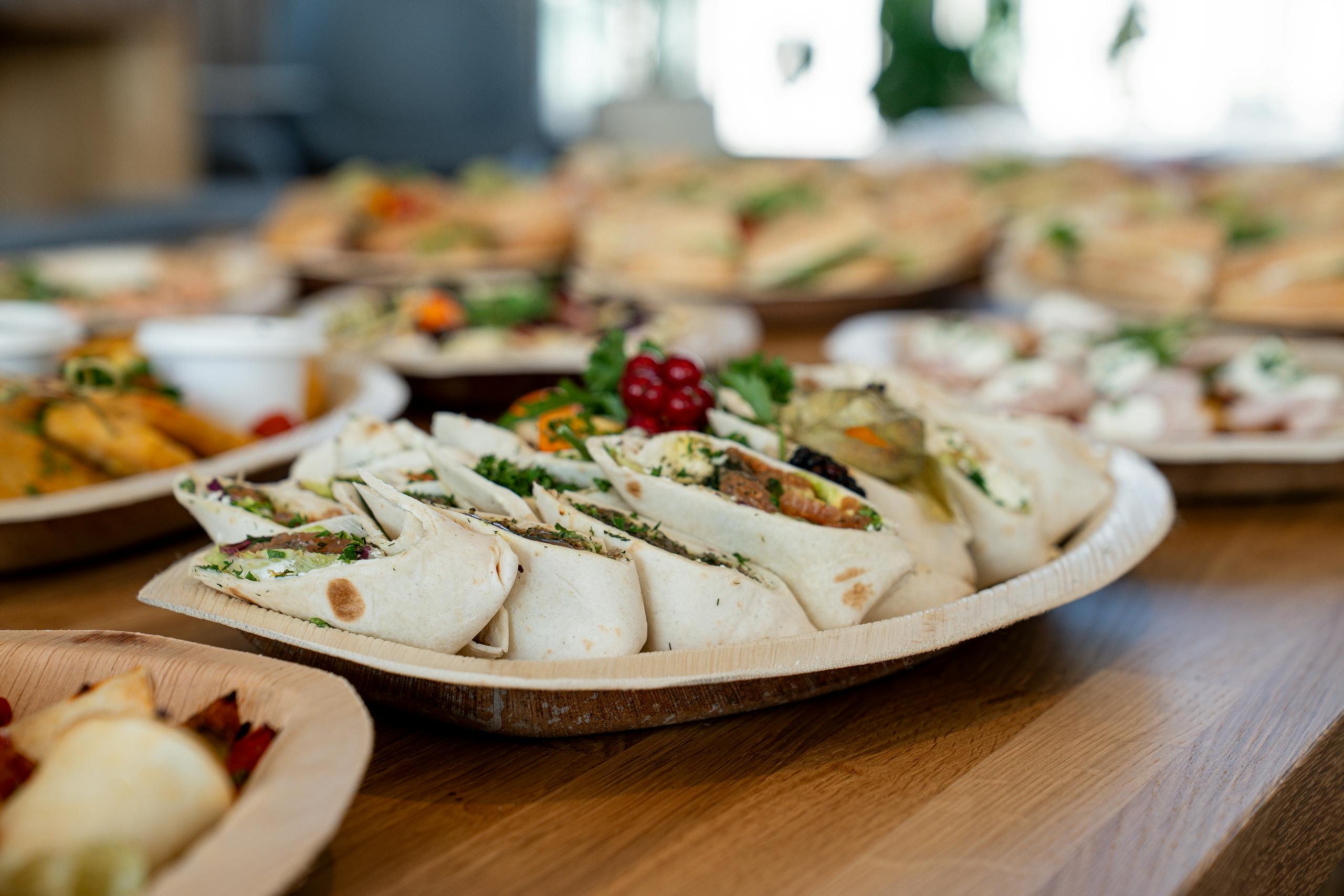 A wooden platter of assorted vegetarian wraps with fresh ingredients, perfect for parties.