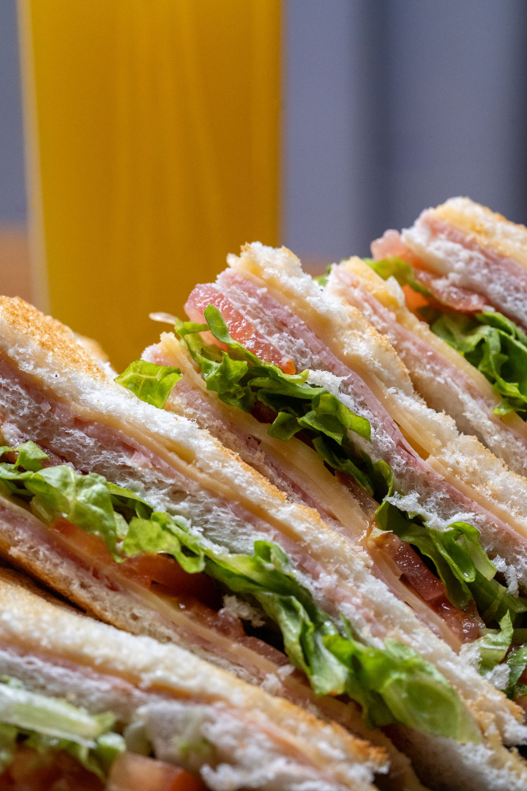 Close-up of a club sandwich with layers of ham, lettuce, tomato, and cheese.