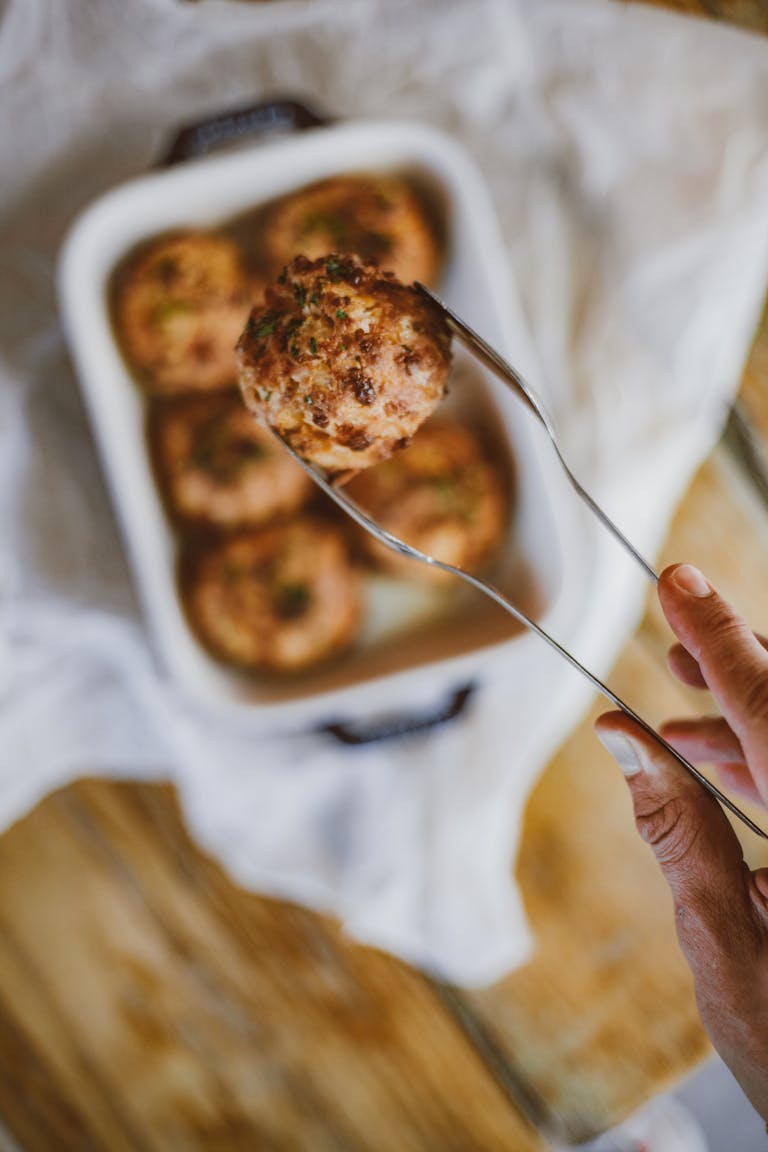Close-up of a hand using tongs to lift freshly baked savory items from a baking dish.