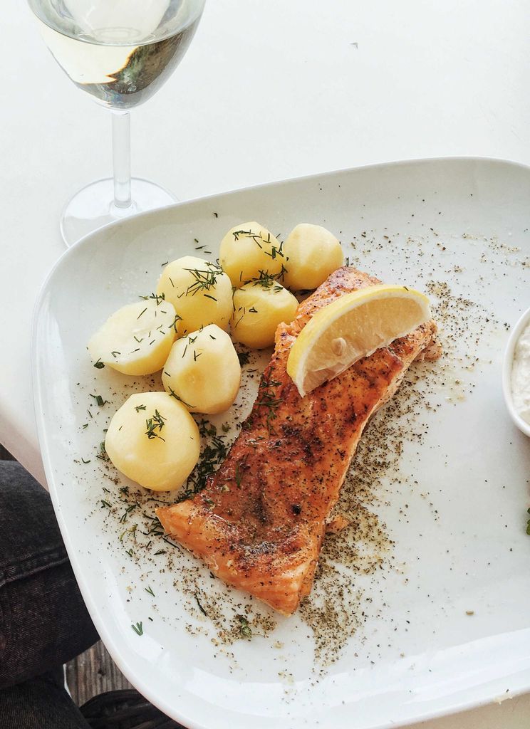 Close-up of baked salmon with potatoes, herbs, and lemon slice on a ceramic plate.
