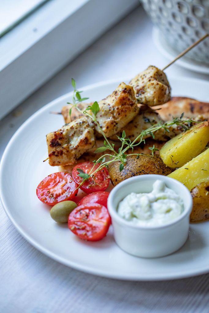 Close-up of grilled chicken kebabs with vegetables and dip on a white plate.