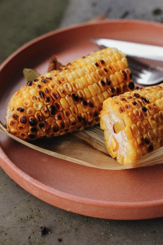 Close-up of grilled corn cobs on a ceramic plate with a rustic feel.