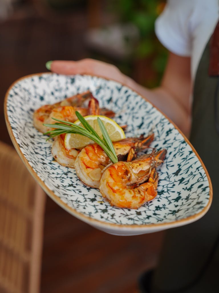 Close-up of grilled prawns garnished with lemon and herbs on a decorative plate.