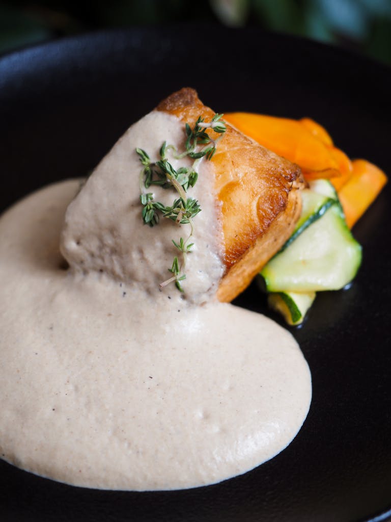 Close-up of seared salmon with creamy sauce and vegetables on a black plate.