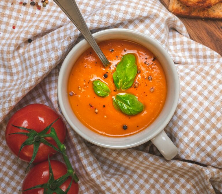 Creamy tomato soup garnished with basil, served with bread and garlic.