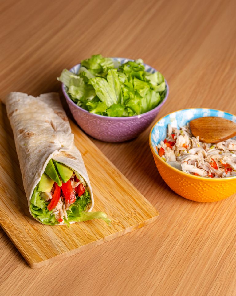 Delicious chicken wrap with fresh vegetables and avocados on a wooden board.