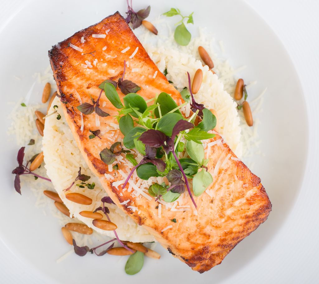 Delicious grilled salmon served with rice, pine nuts, and microgreens on a white plate.