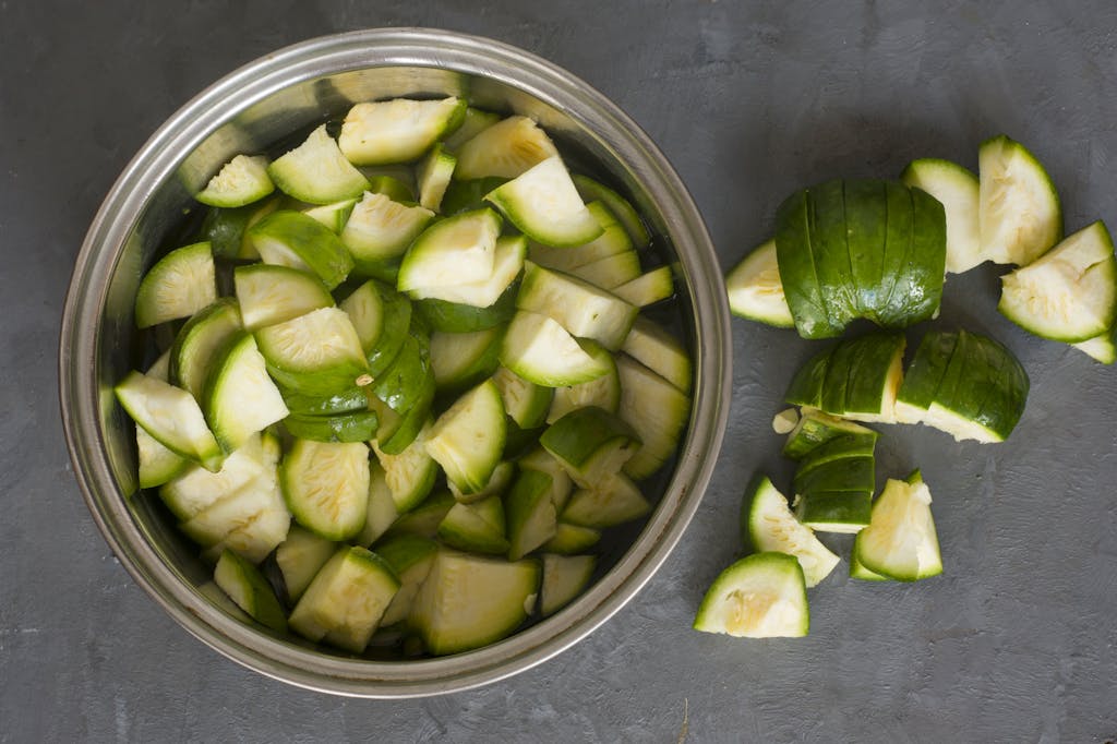 Fresh chopped courgettes in a metal bowl on a gray countertop, showcasing healthy, nutritious vegetables.