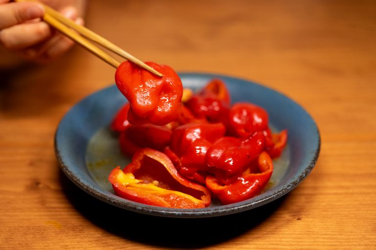 Fresh red bell pepper slices served on a blue plate, lifted with chopsticks for a gourmet presentation.