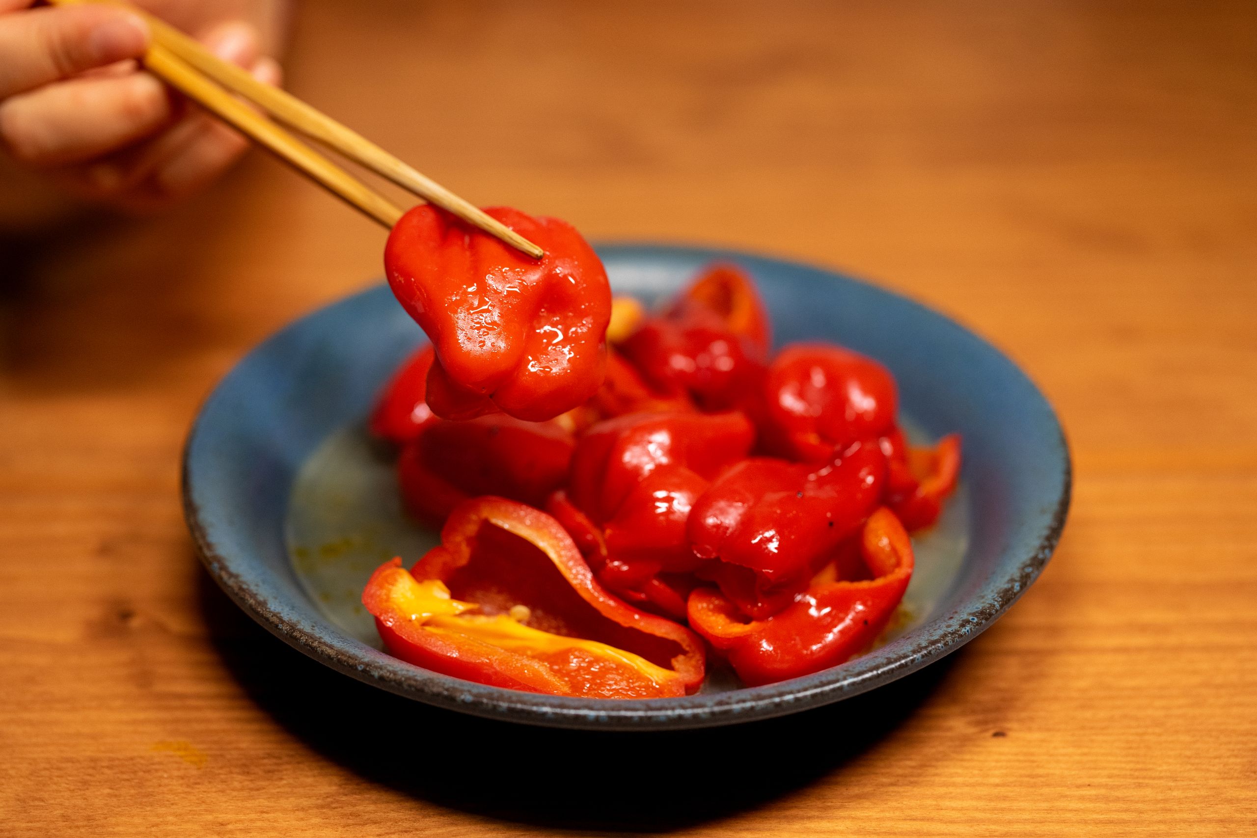 Fresh red bell pepper slices served on a blue plate, lifted with chopsticks for a gourmet presentation.