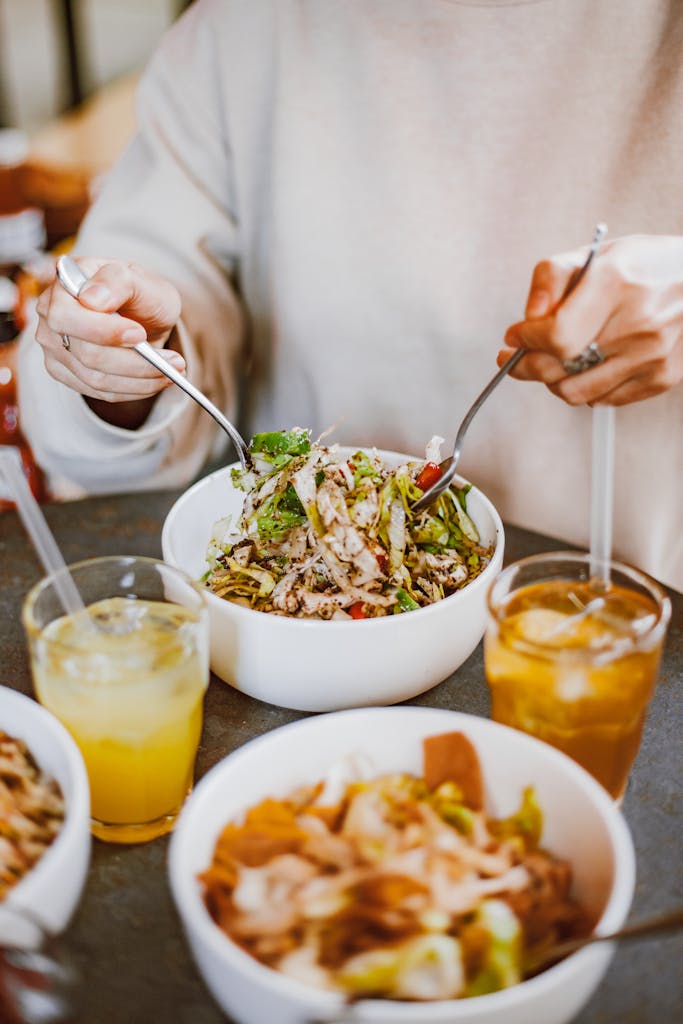Fresh salad in a bowl with hands tossing it, accompanied by refreshing juices, perfect for a healthy meal.