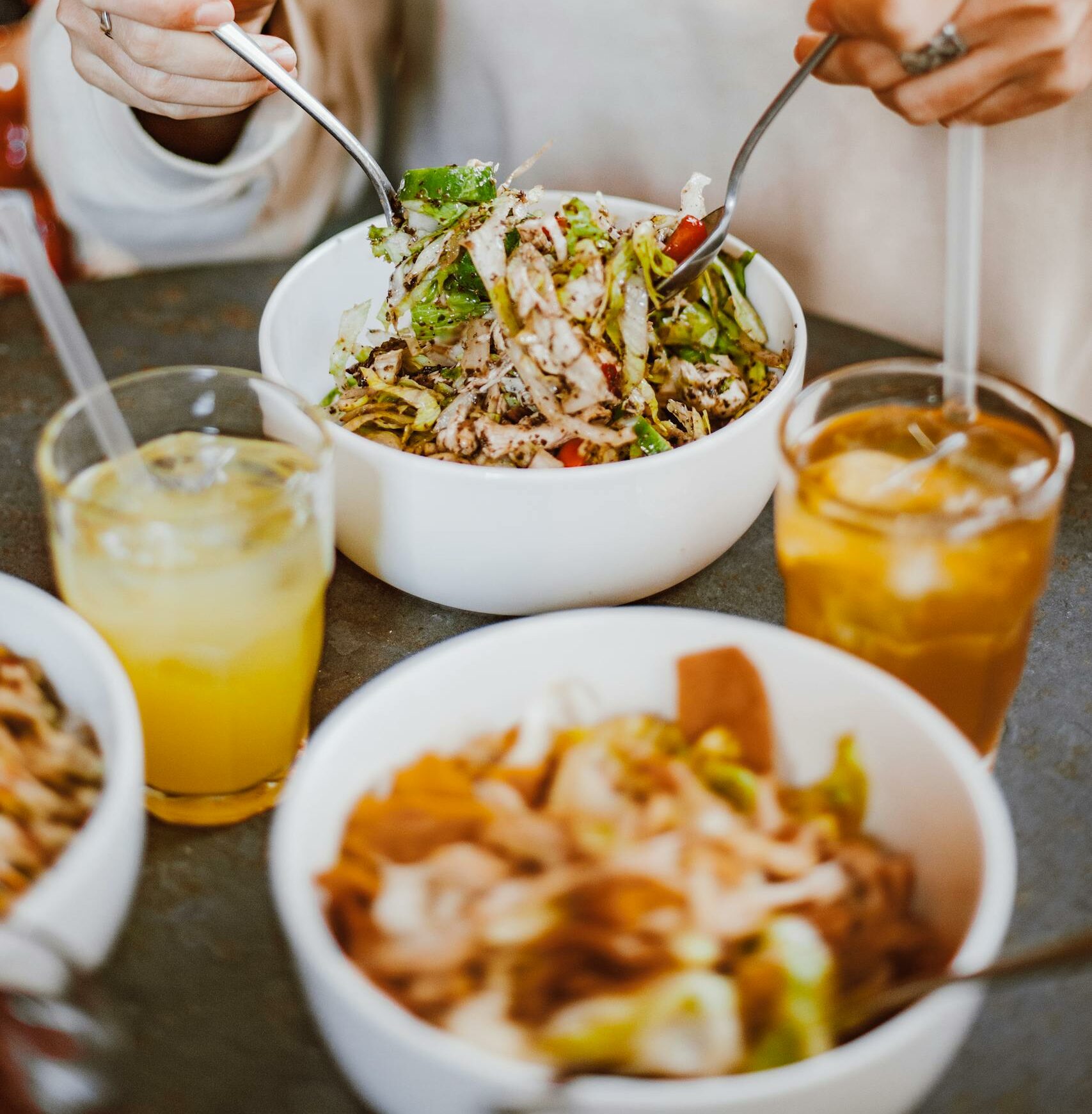 Fresh salad in a bowl with hands tossing it, accompanied by refreshing juices, perfect for a healthy meal.