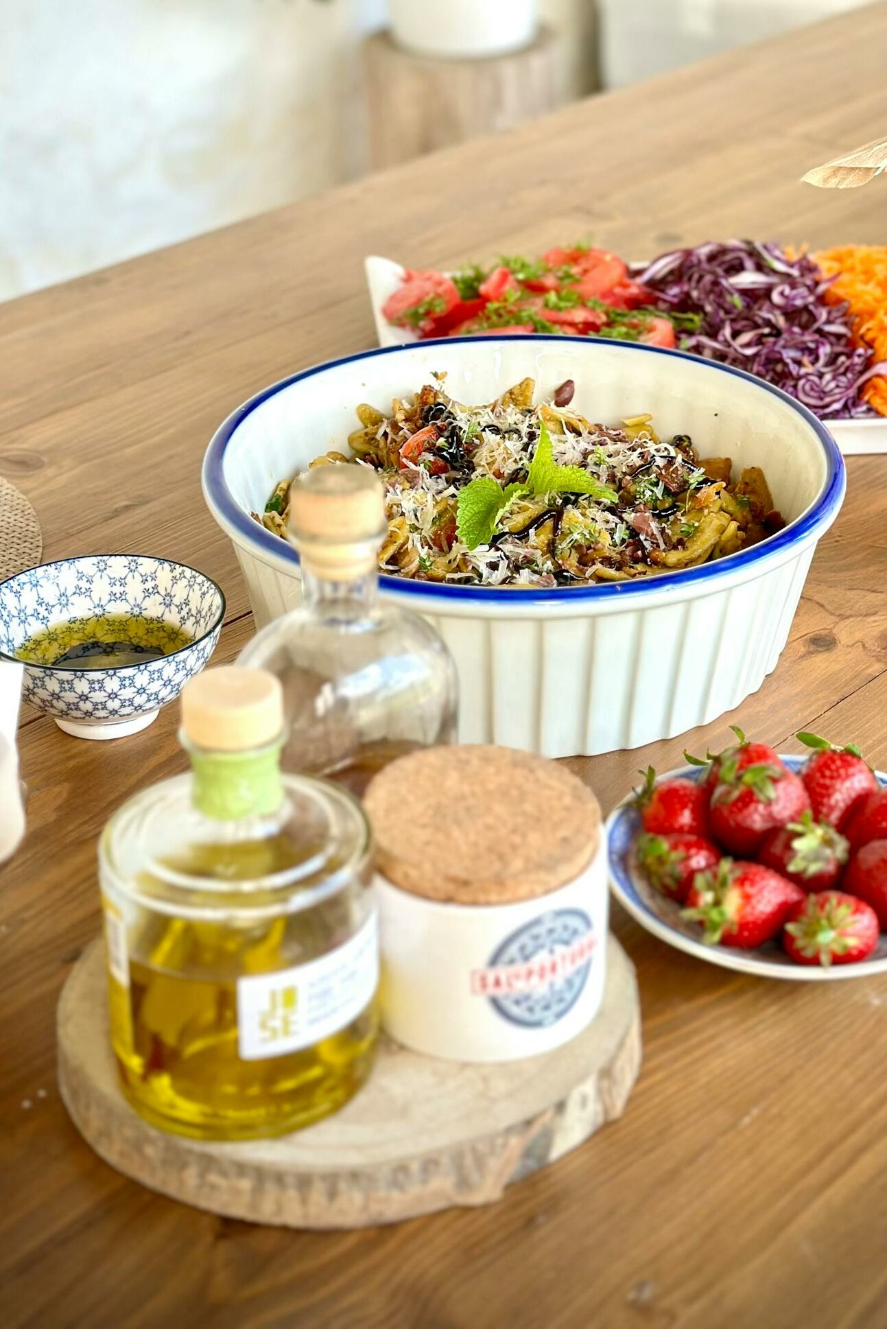 Fresh summer salad and strawberries on a rustic table with wine and olive oil.