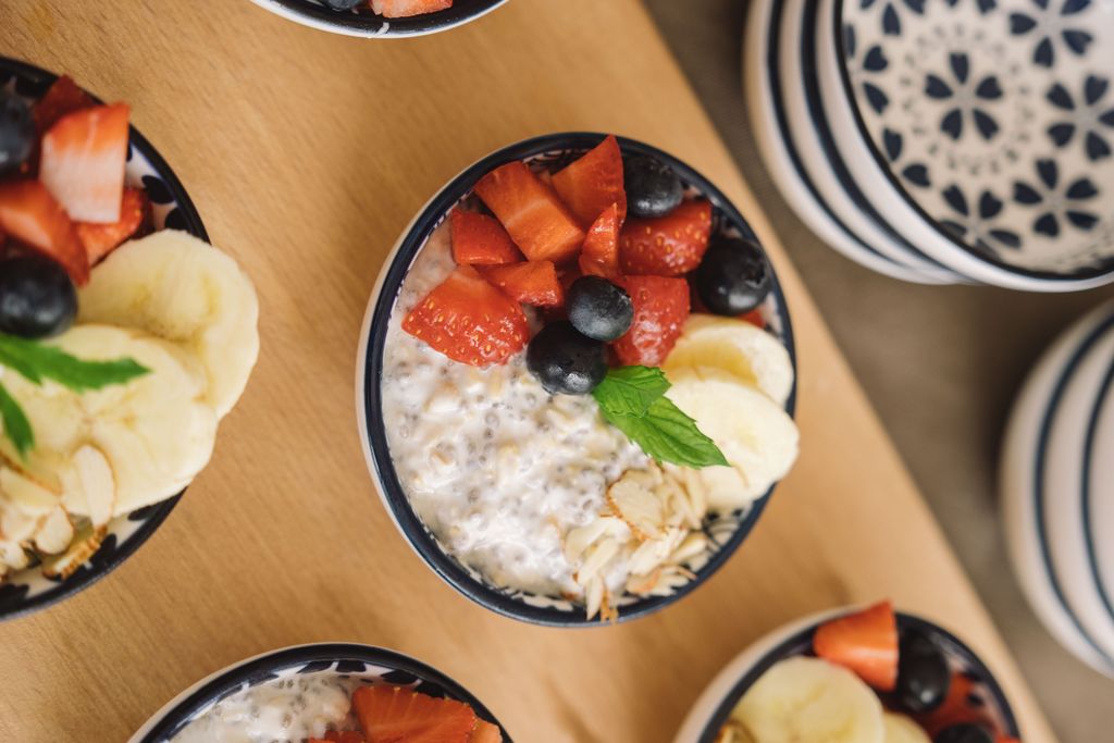 Overhead view of oatmeal bowls topped with fresh fruits like bananas, strawberries, and blueberries.