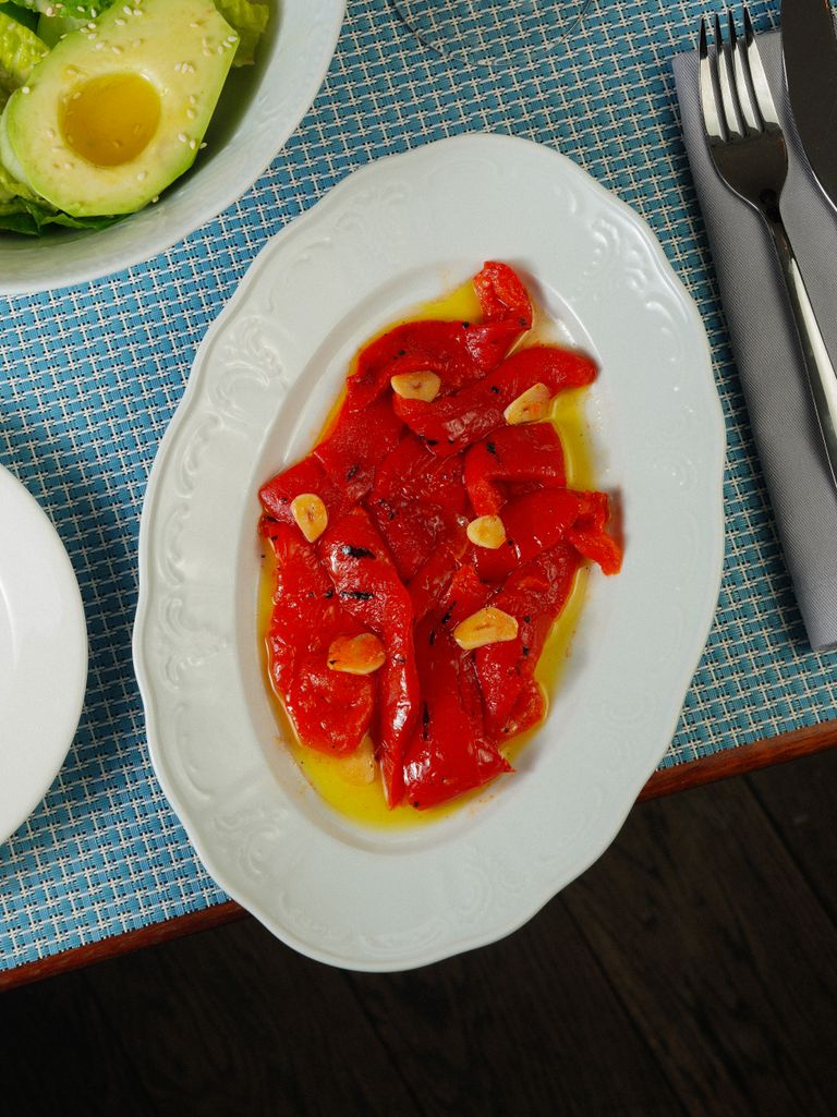Plate of roasted red peppers with garlic and olive oil on a table.