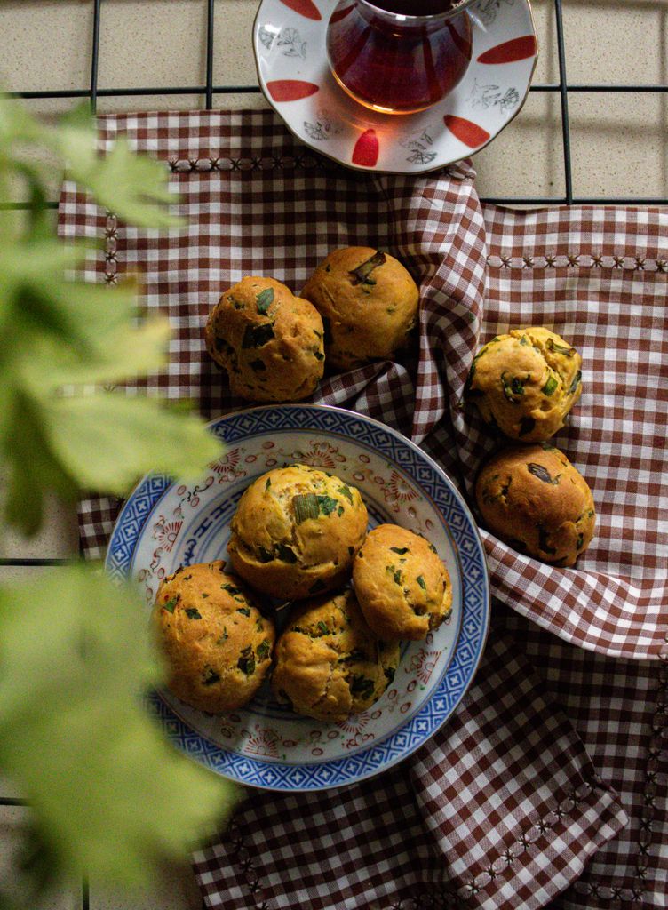 Rustic setup of herb muffins on a checkered cloth beside a glass of tea.