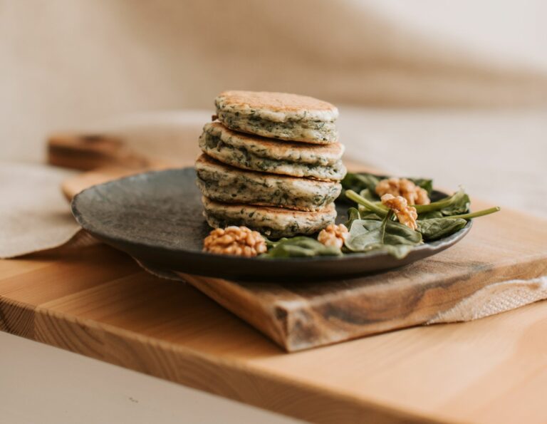 Savory pancakes stacked on a rustic plate with spinach and walnuts, perfect breakfast setting.