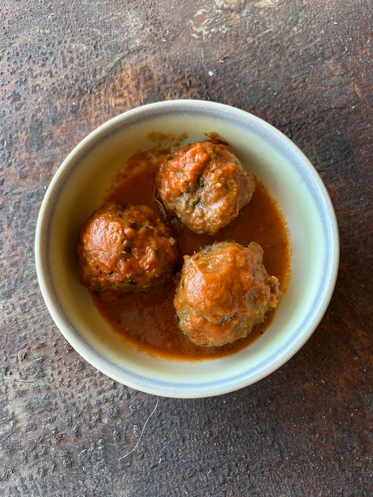 Three tasty meatballs in rich tomato sauce in a ceramic bowl, perfect for comfort food enthusiasts.