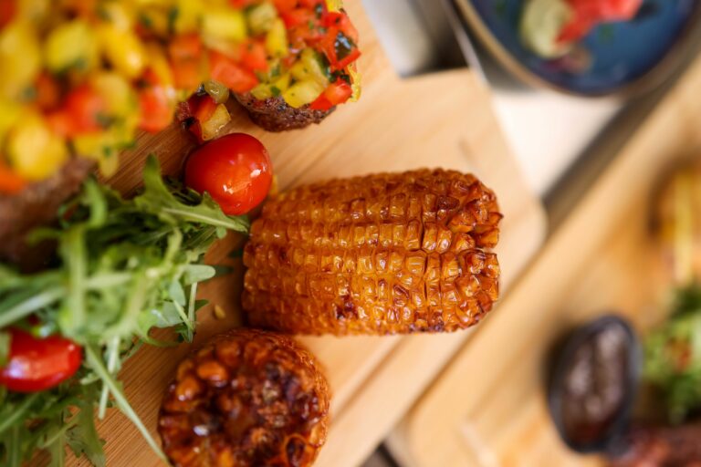 Vertical shot of grilled corn on cutting board with fresh salad and veggies.