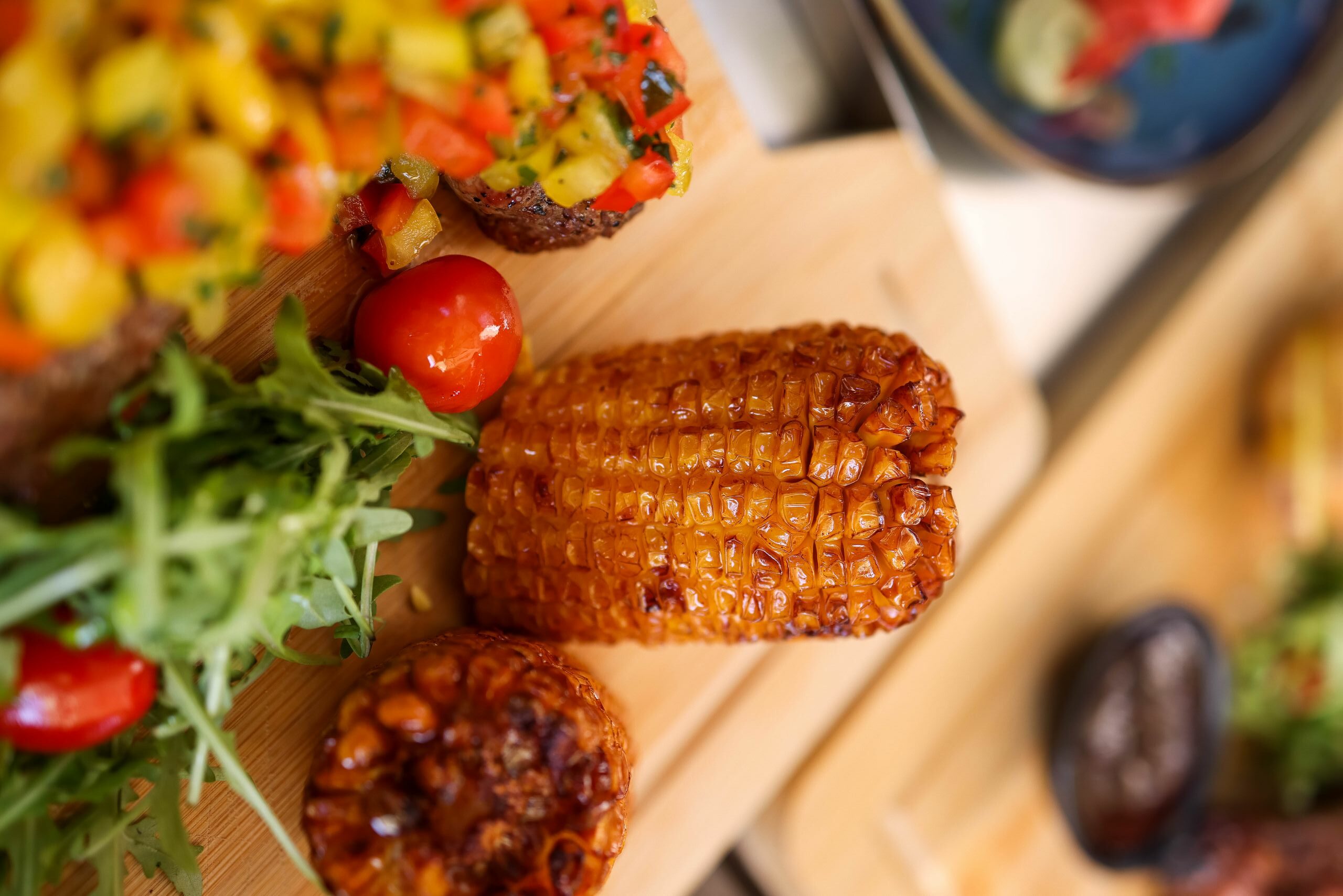 Vertical shot of grilled corn on cutting board with fresh salad and veggies.
