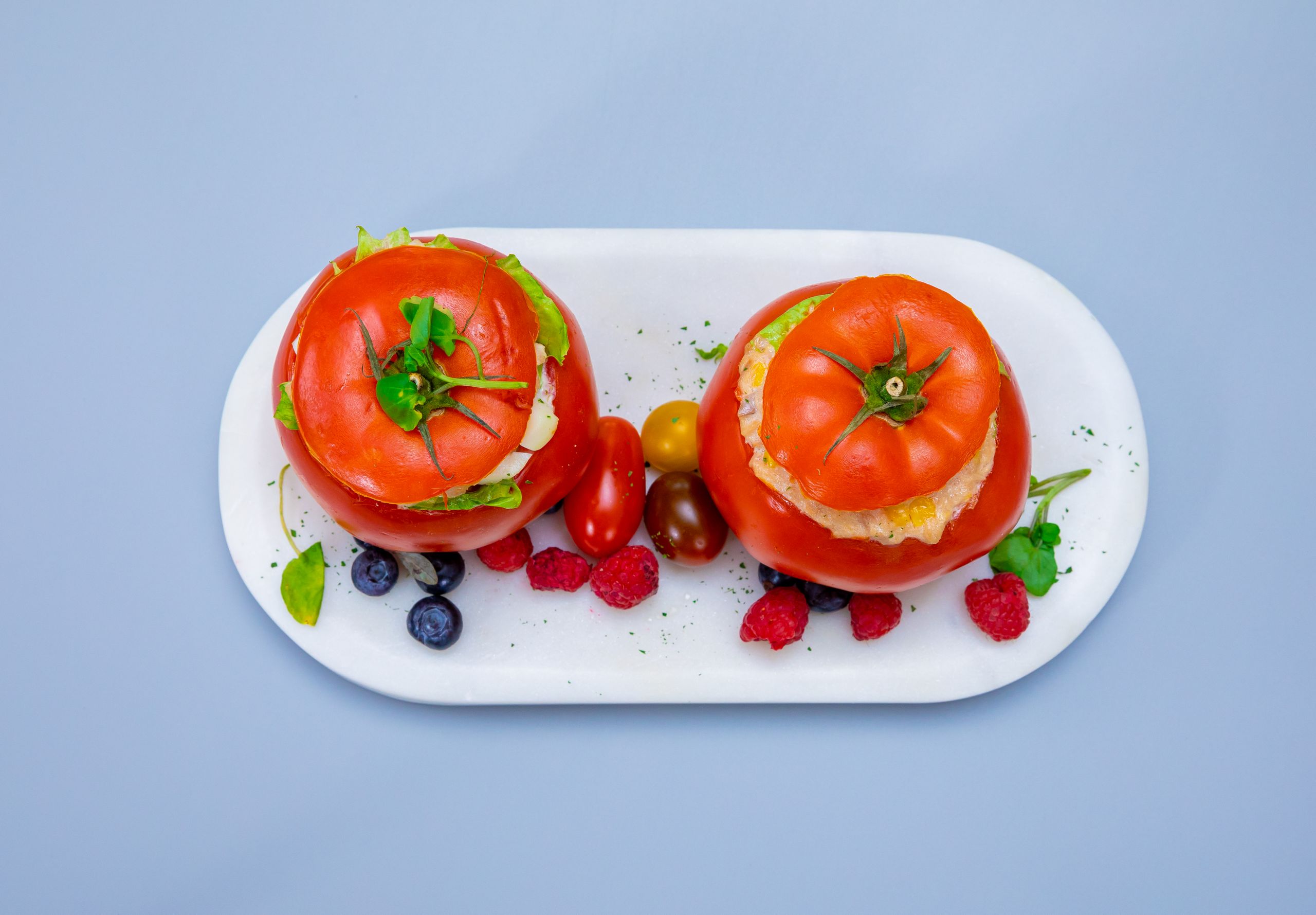 Vibrant stuffed tomatoes with berries on a blue background, showcasing fresh, healthy food.