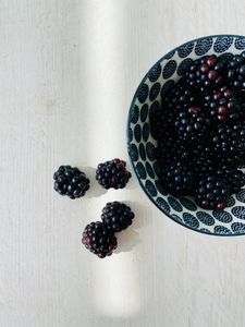 A close-up of fresh blackberries in a decorative bowl on a light wooden table, showcasing their juicy texture.