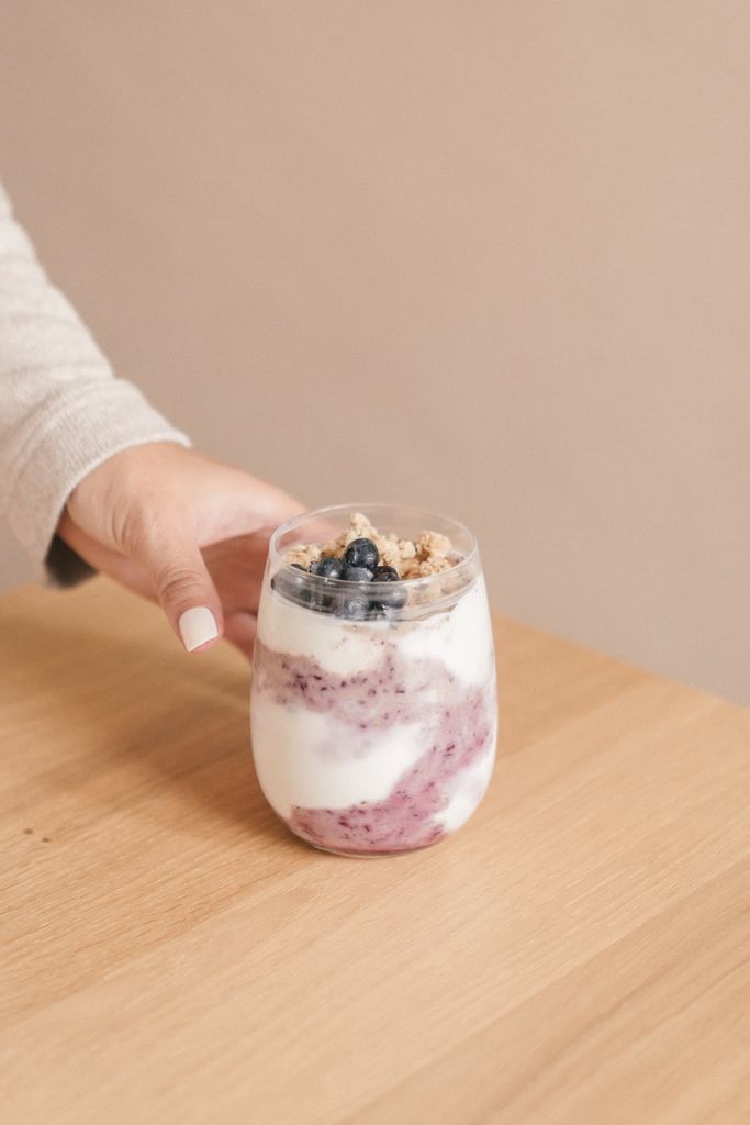 A creamy yogurt parfait topped with fresh blueberries and crunchy granola, hand-held on a wooden table.