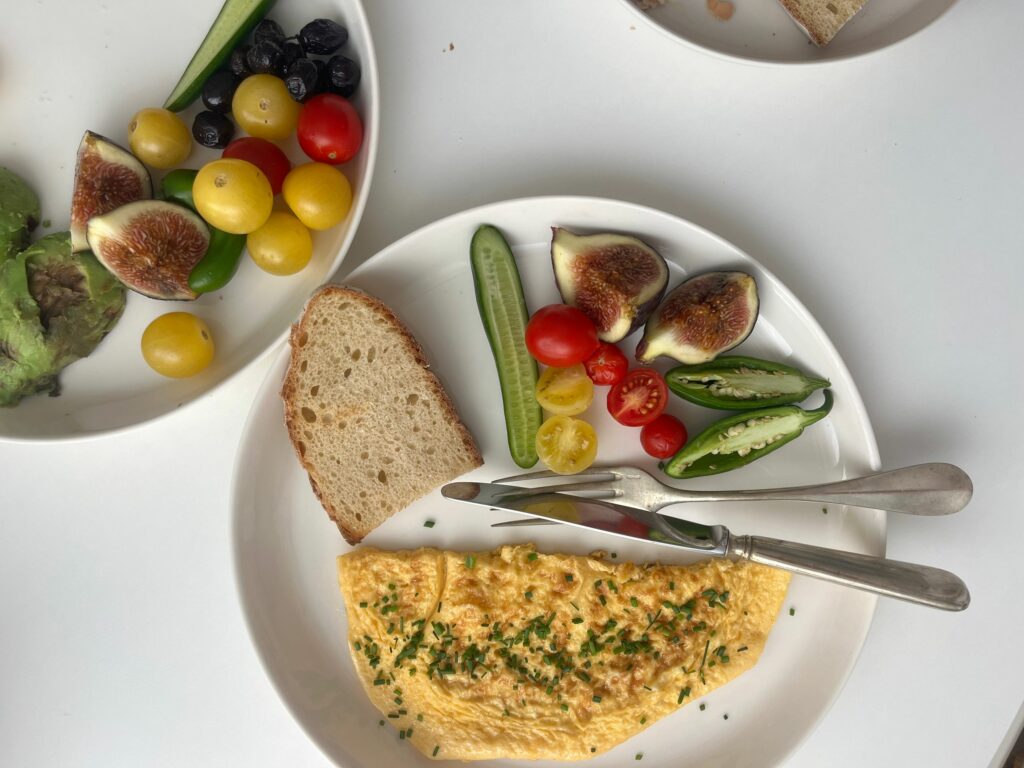 A vibrant breakfast featuring omelette, fresh vegetables, figs, and bread on a white plate.