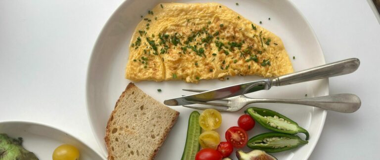 A vibrant breakfast featuring omelette, fresh vegetables, figs, and bread on a white plate.