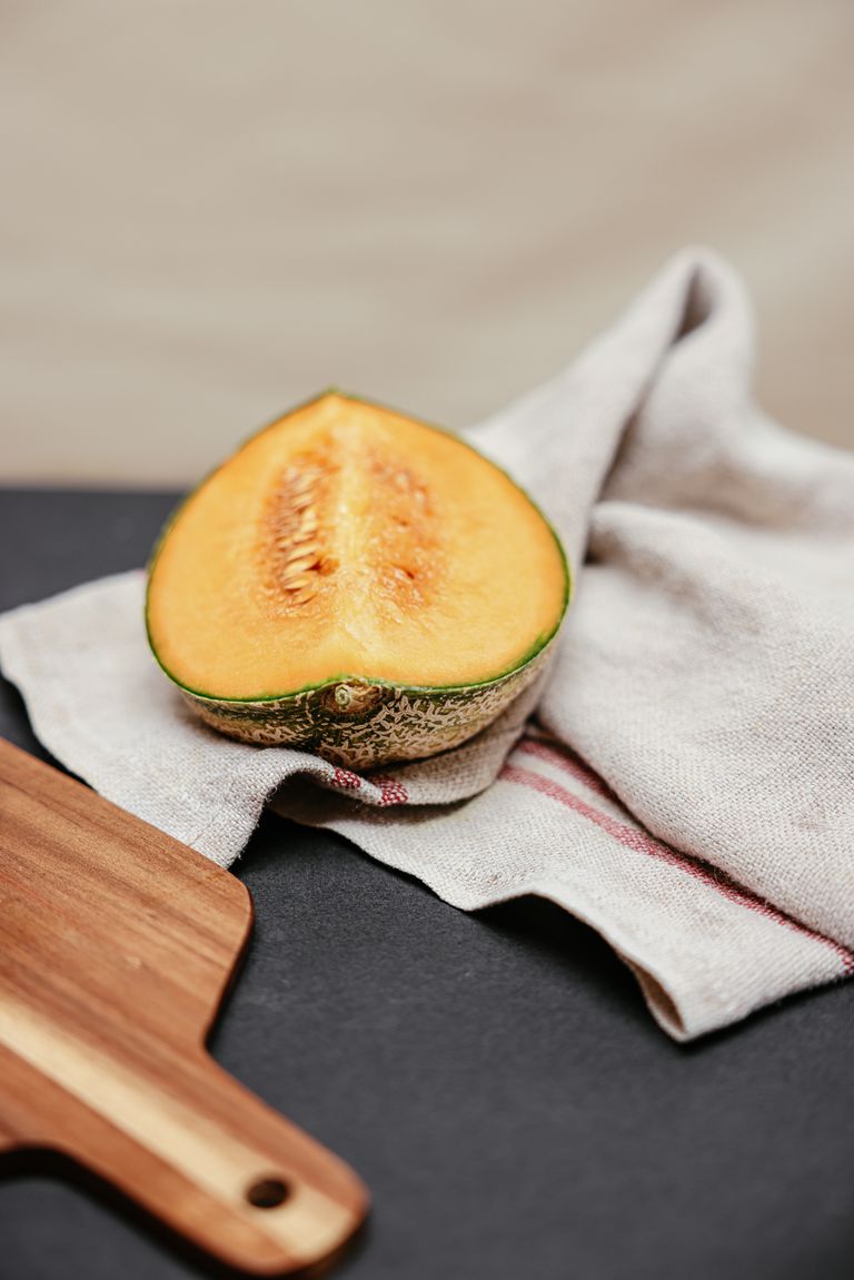 Artistic close-up of a sliced melon on a linen cloth with a wooden board.