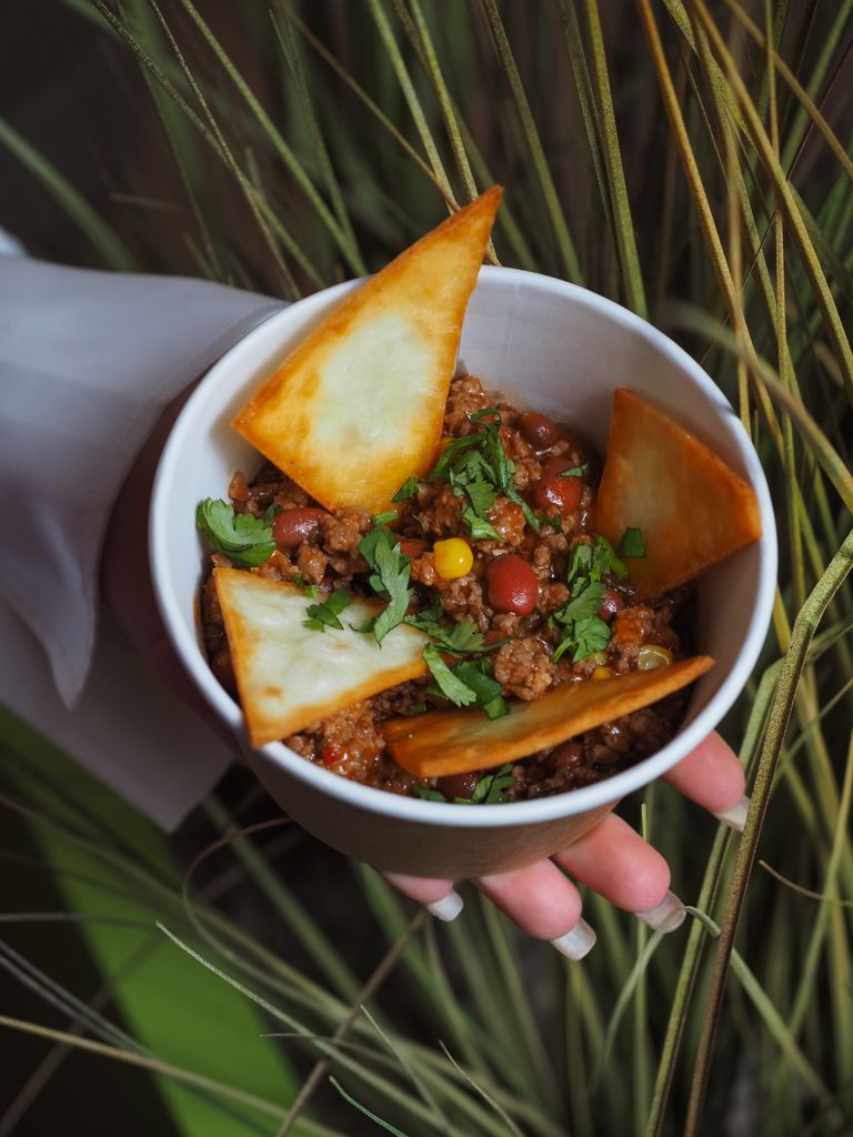 Bowl of chili con carne topped with crispy tortilla chips and fresh coriander.