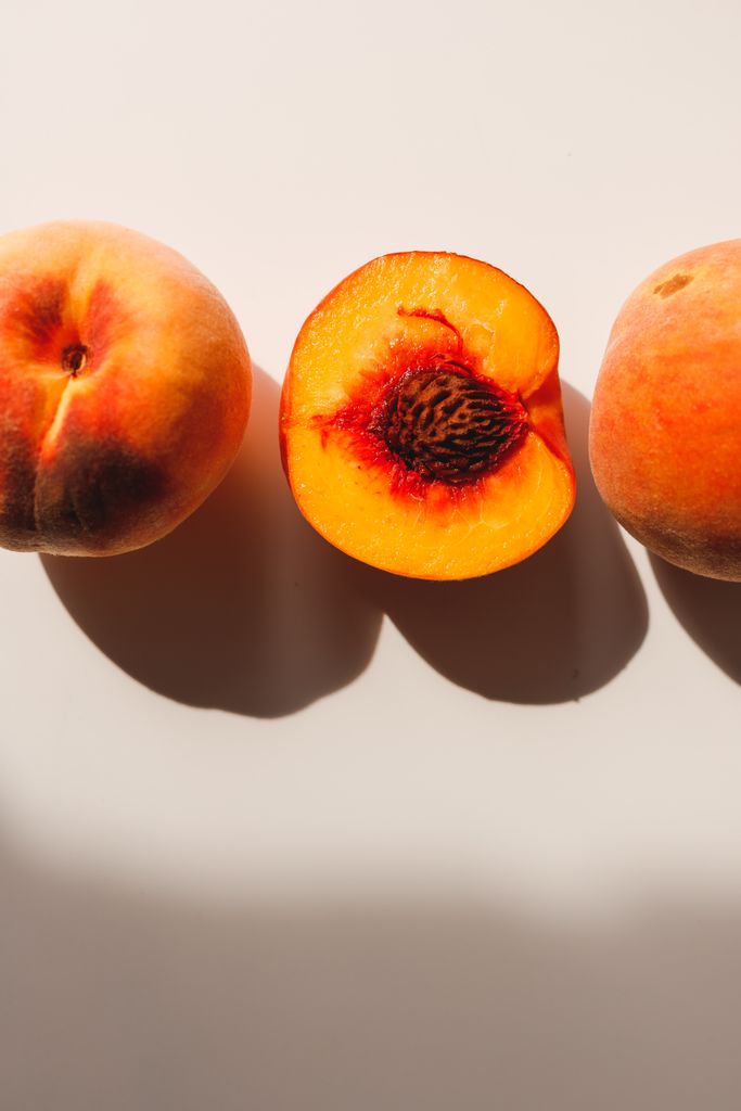 Bright and vibrant peaches with a sliced half showcasing their juicy texture, casting shadows.