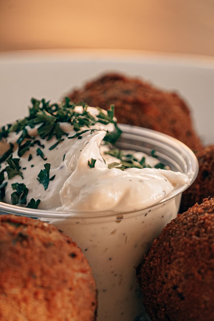 Close-up of falafel balls with creamy tzatziki sauce in a bowl, garnished with herbs.