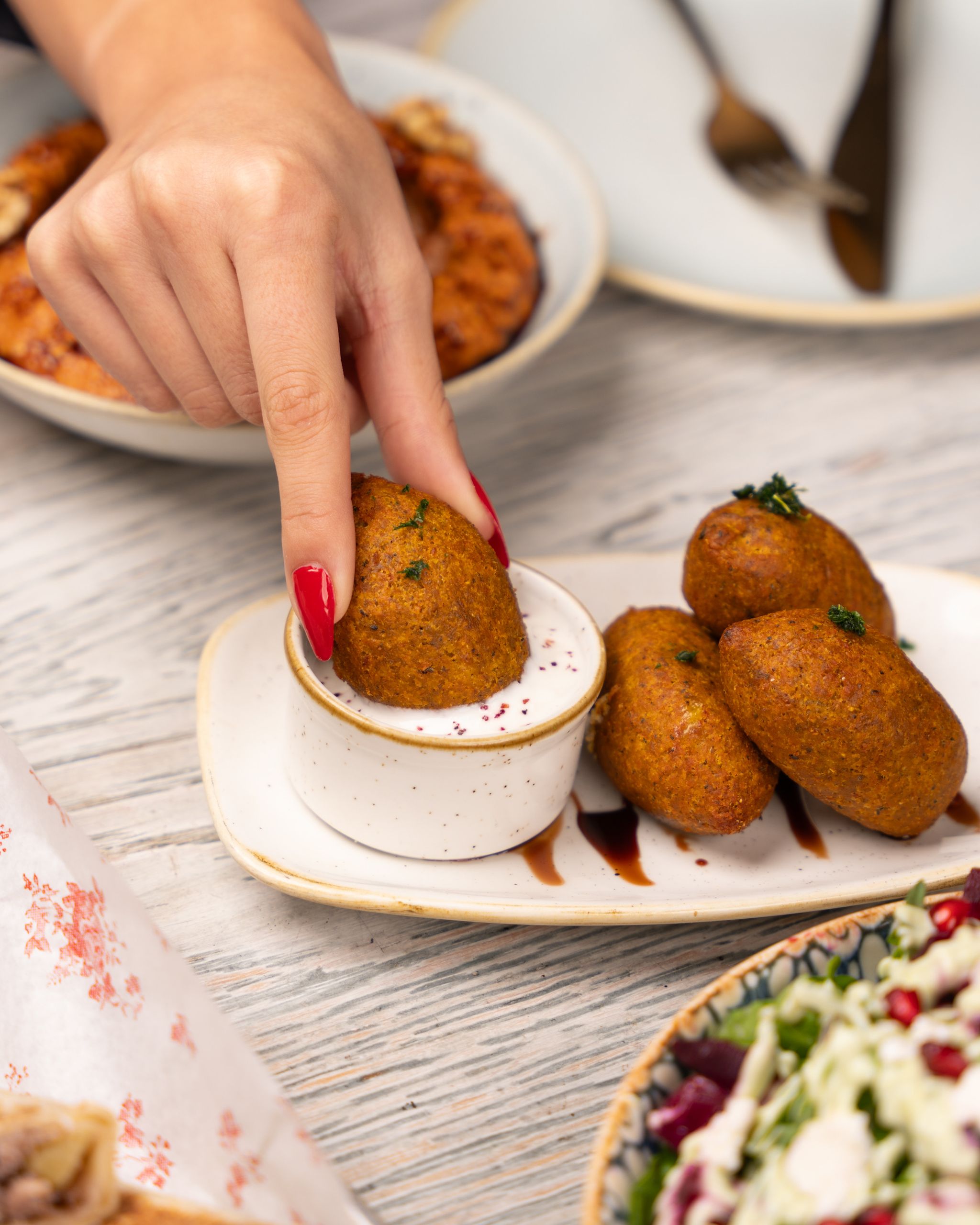 Close-up of falafel being dipped in sauce, surrounded by Middle Eastern dishes.