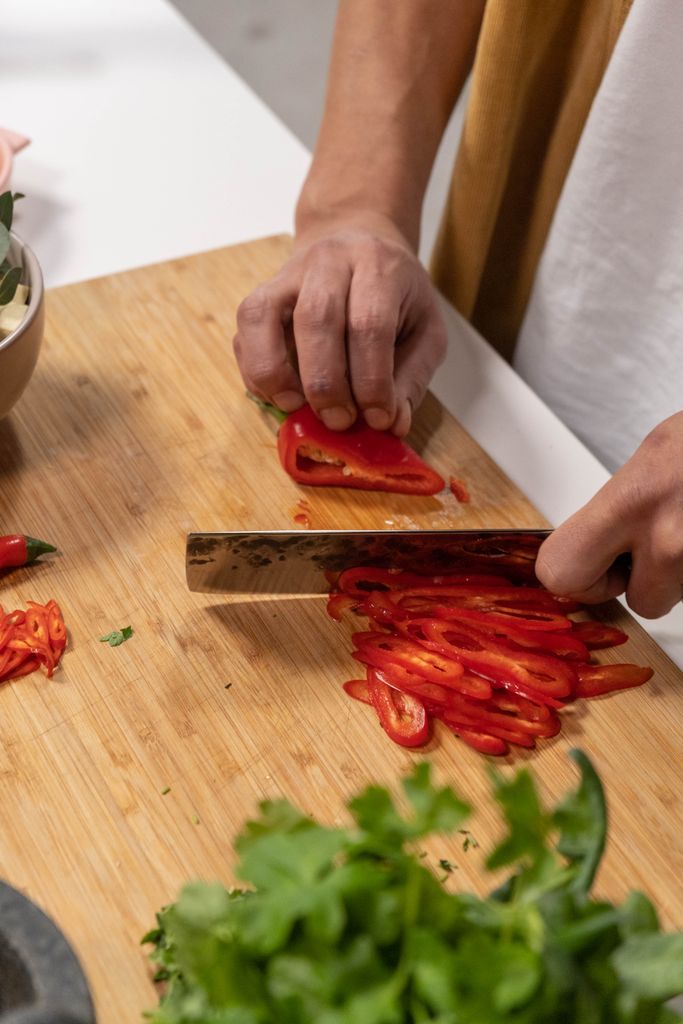 Close-up of hands slicing vibrant red peppers on a wooden chopping board. Perfect for food and cooking themes.