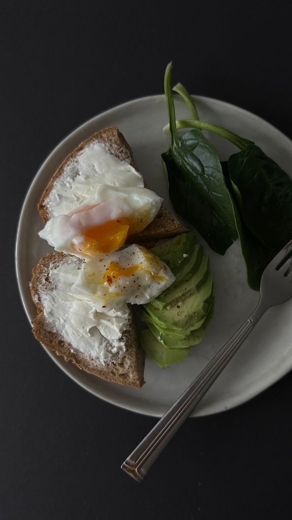 Delicious avocado toast topped with a fried egg and fresh spinach on a plate.