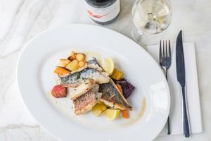 Elegant fish dish paired with white wine, presented on a marble table setting.