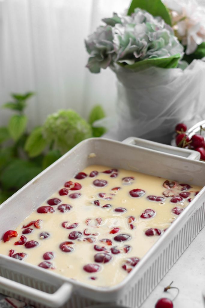 Freshly prepared cherry clafoutis in a white dish, ready for baking with natural light.