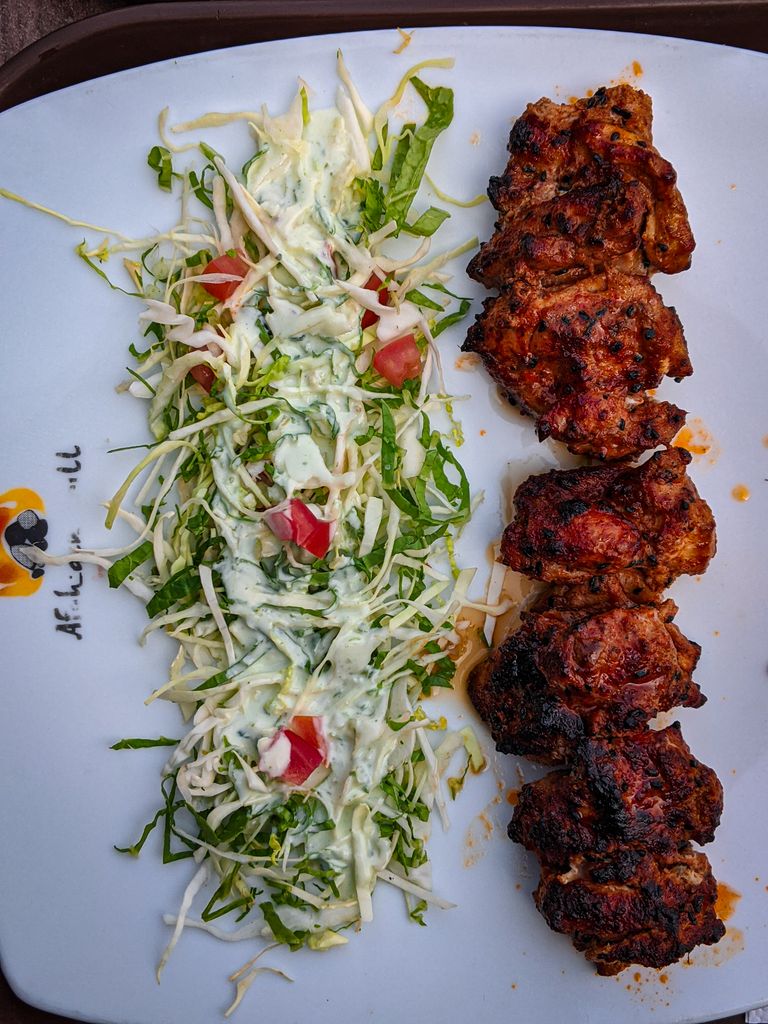 Grilled meat served with fresh salad on a decorative white plate, perfect for a tasty meal.