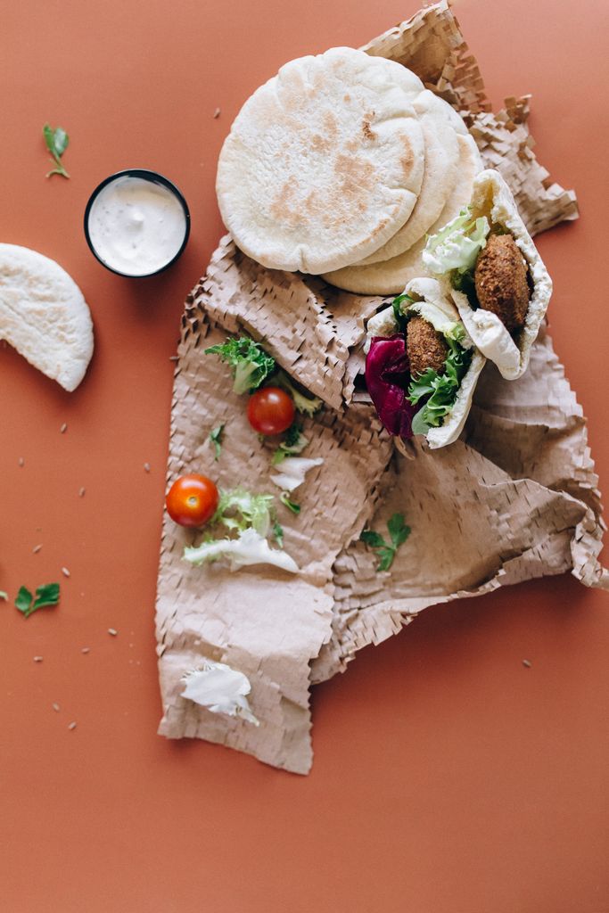 High angle view of falafel wraps with cherry tomatoes and sauce on paper.