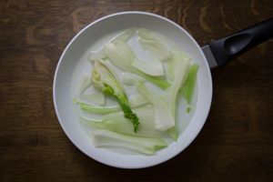 Overhead view of fresh fennel slices in a white frying pan. Perfect for healthy cooking concepts.