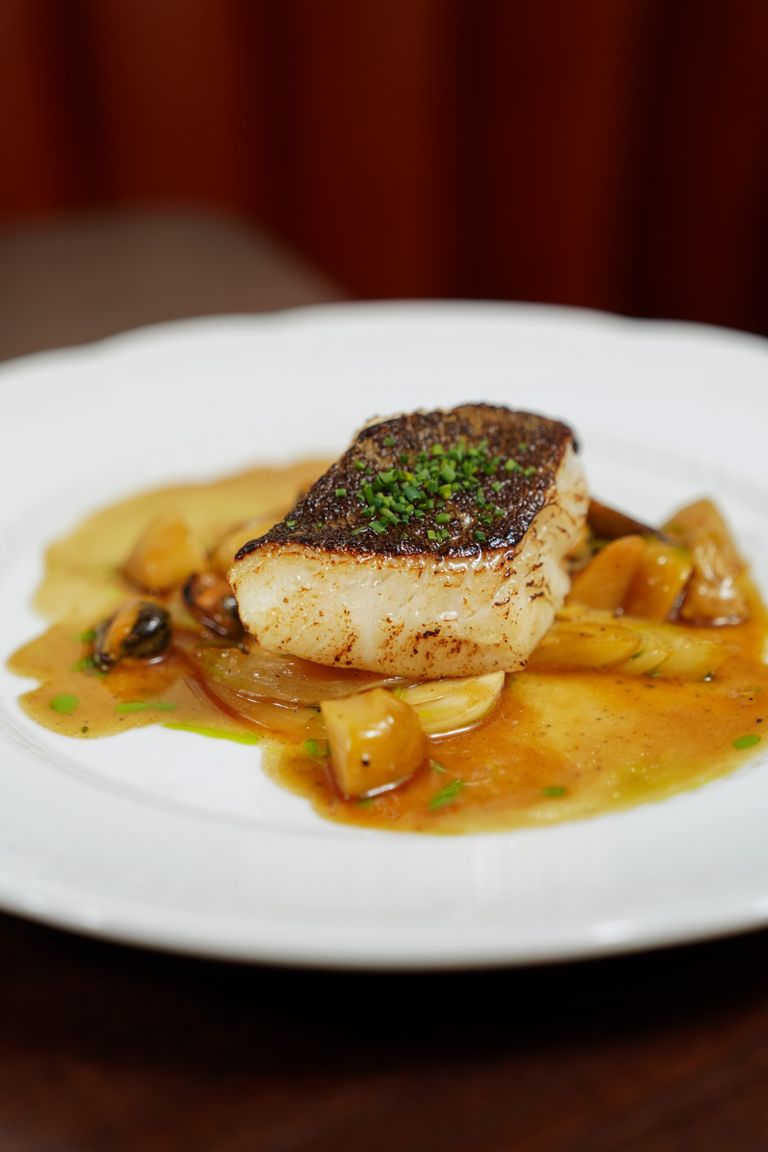 Pan-seared fish on a white plate with garnish in a fine dining setting.