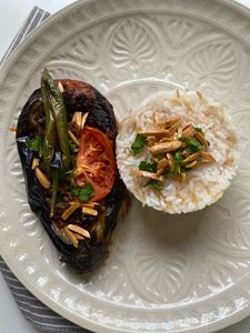 Savor the flavors of eggplant and rice garnished with tomatoes and almonds on a decorative plate.