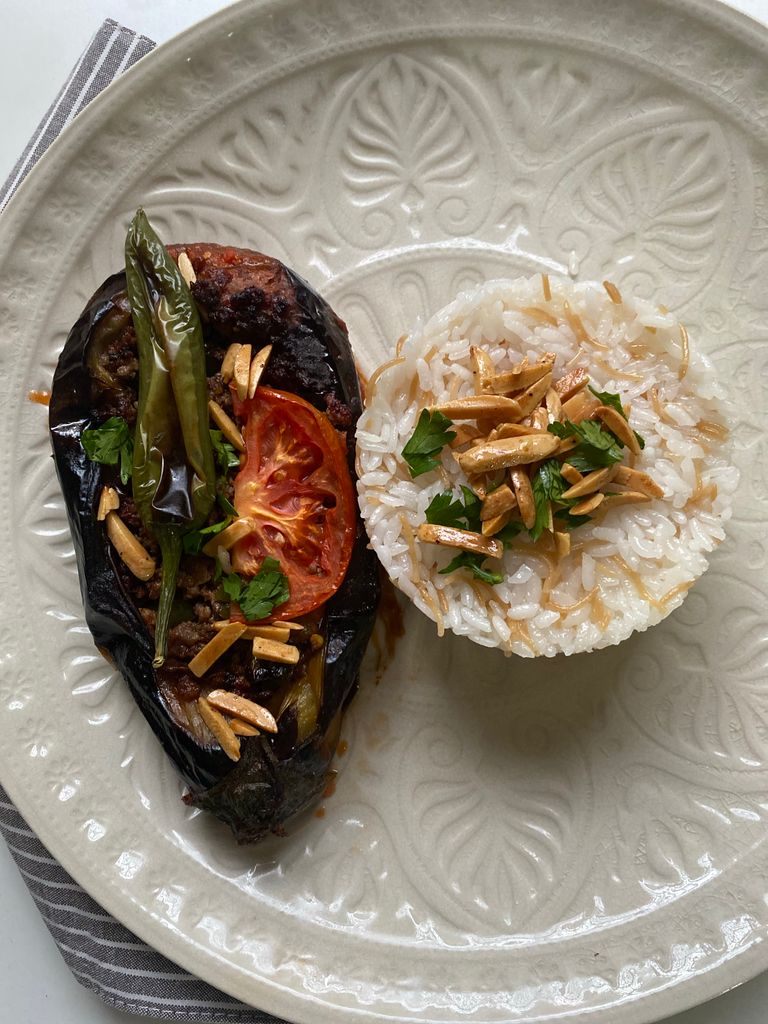 Savor the flavors of eggplant and rice garnished with tomatoes and almonds on a decorative plate.