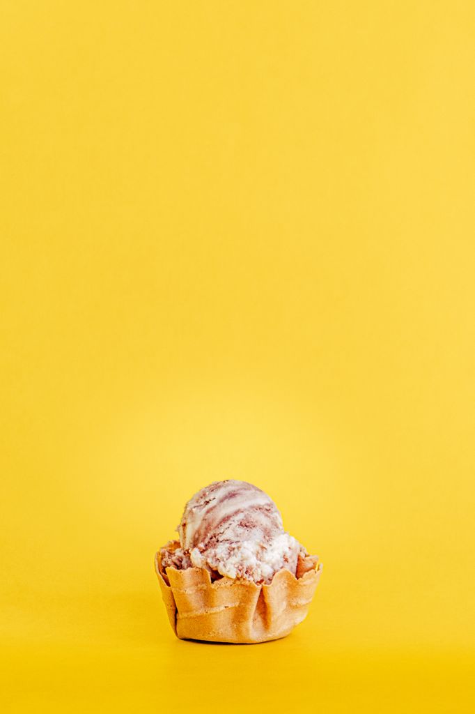 Single scoop of chocolate ice cream in a waffle cup against a vibrant yellow backdrop.